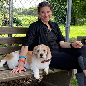 Photo of woman sitting on bench with a brown and white dog laying next to her. 