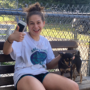 Volunteer sitting on bench petting small black and tan dog, taking a selfie